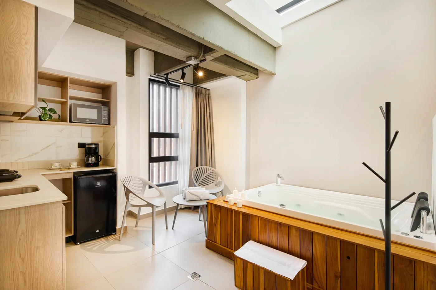 Suite con tina de hidromasaje revestida en madera, cocineta y sillas junto a la ventana