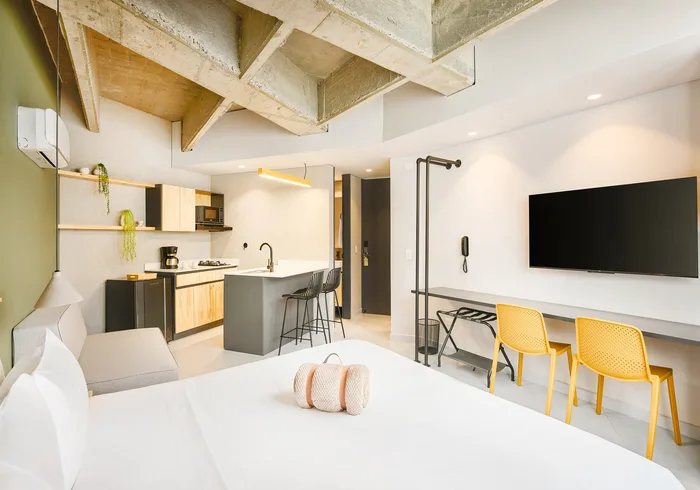 Suite Superior: cama, cocineta con barra, TV y escritorio con sillas amarillas
