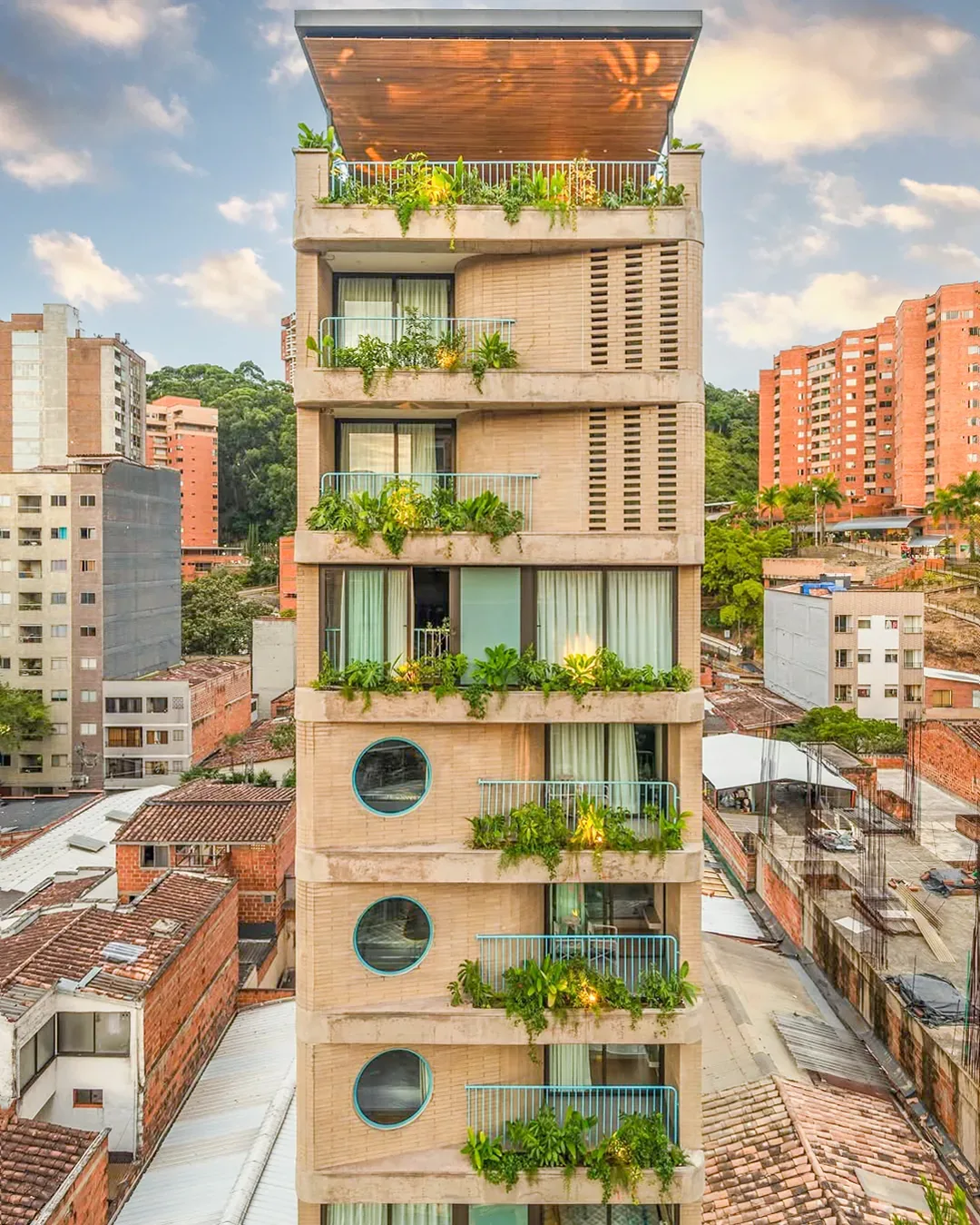 Torre de ladrillo de Once22 con balcones llenos de plantas y ventanas redondas, en Sabaneta